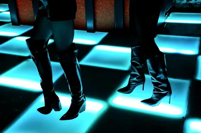 Dancers on the lit checkerboard floor at Ciao Ciao Disco, a mirror ball and neon tubing under the brick vault