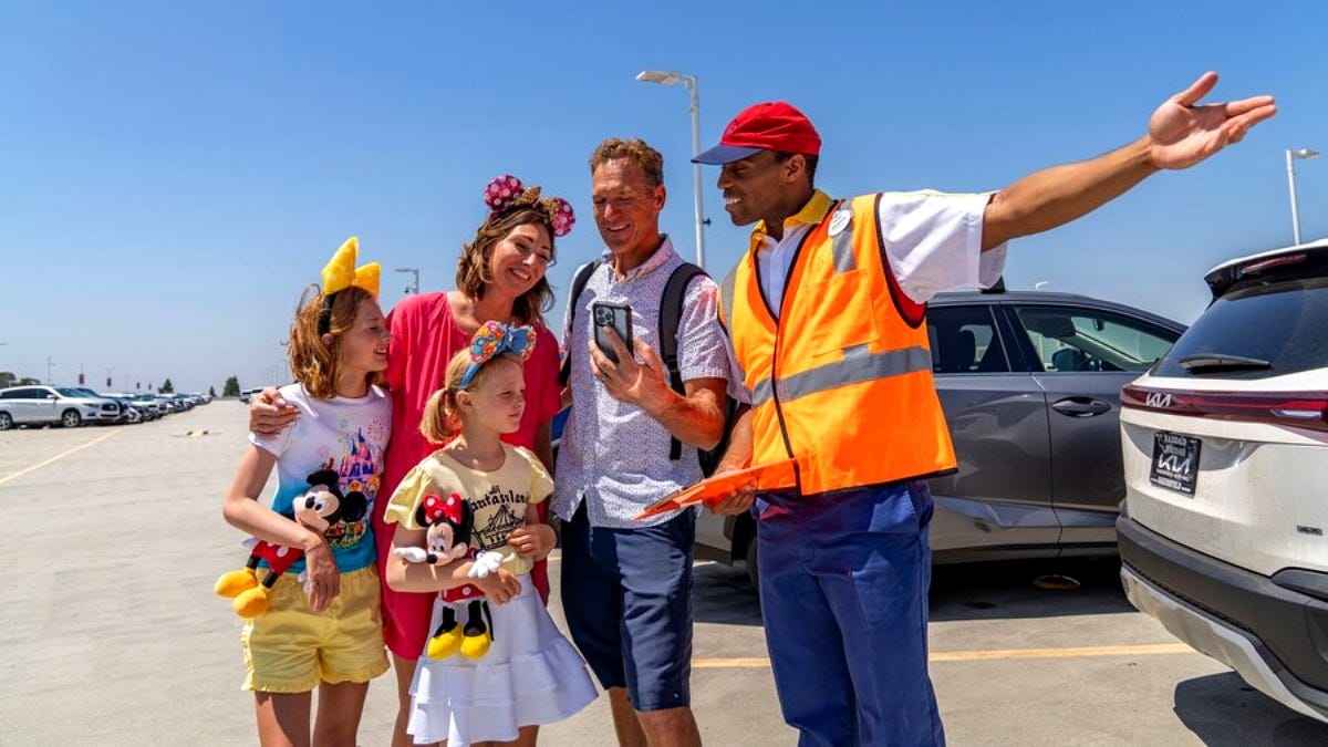 A Disneyland Resort cast member gives a family directions in a parking area. Image: Disney