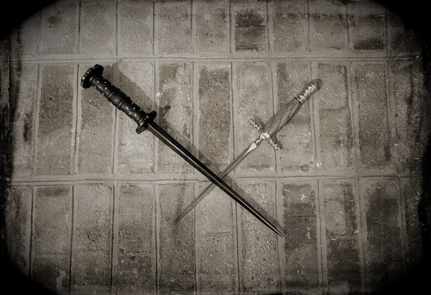 A sepia-toned photo made to look like a Victorian era daguerreotype. The photo shows two daggers crossed against a brick background.