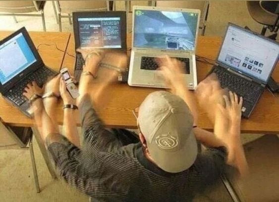 This may contain: a man sitting at a table with three laptops and two phones in front of him