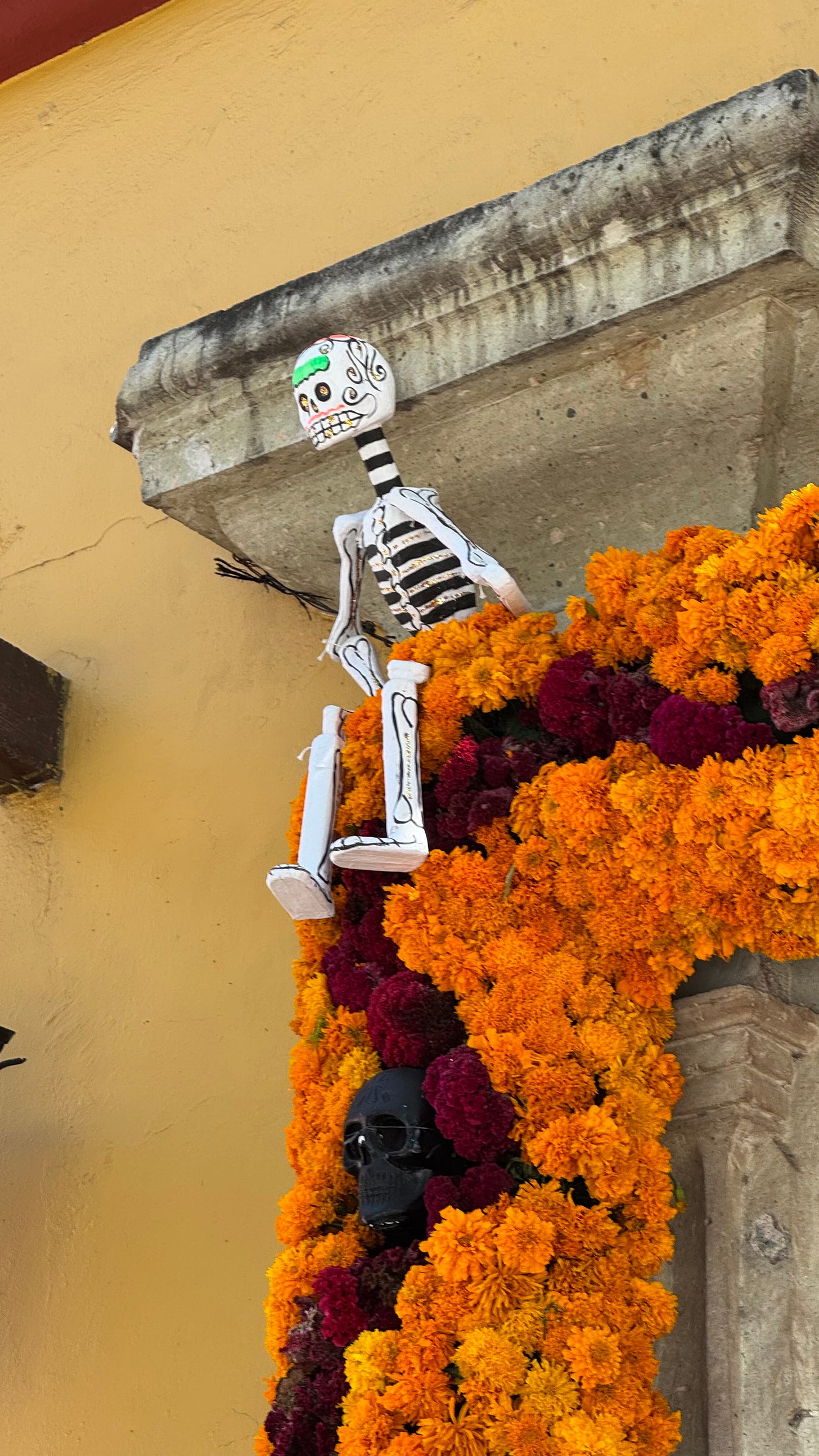 A stone doorway lined with flowers with a skeleton perched on the eve.