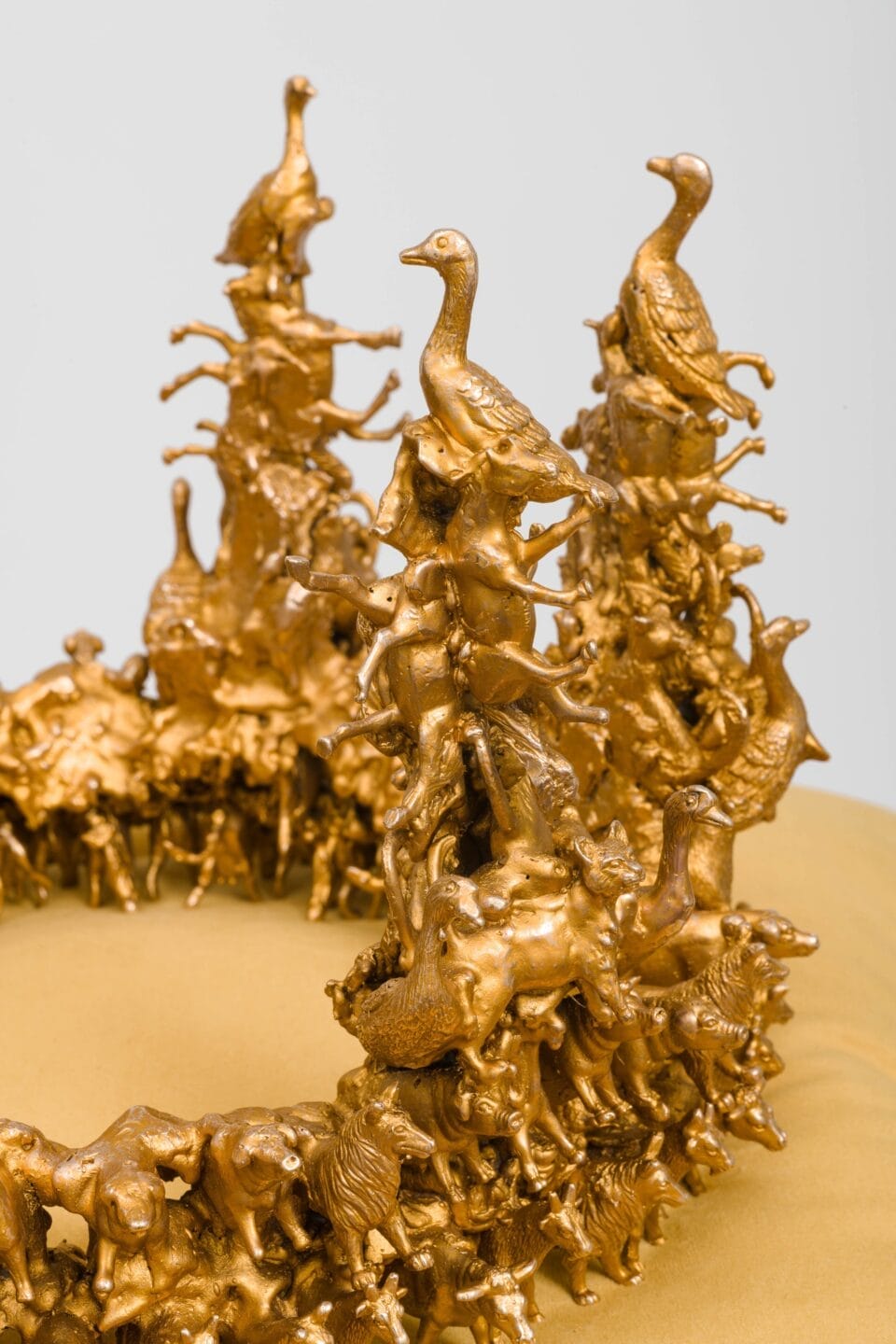 a detail of a sculpture of a gold-coated bronze crown composed of tiny birds and other animals, situated on yellow velvet cushion