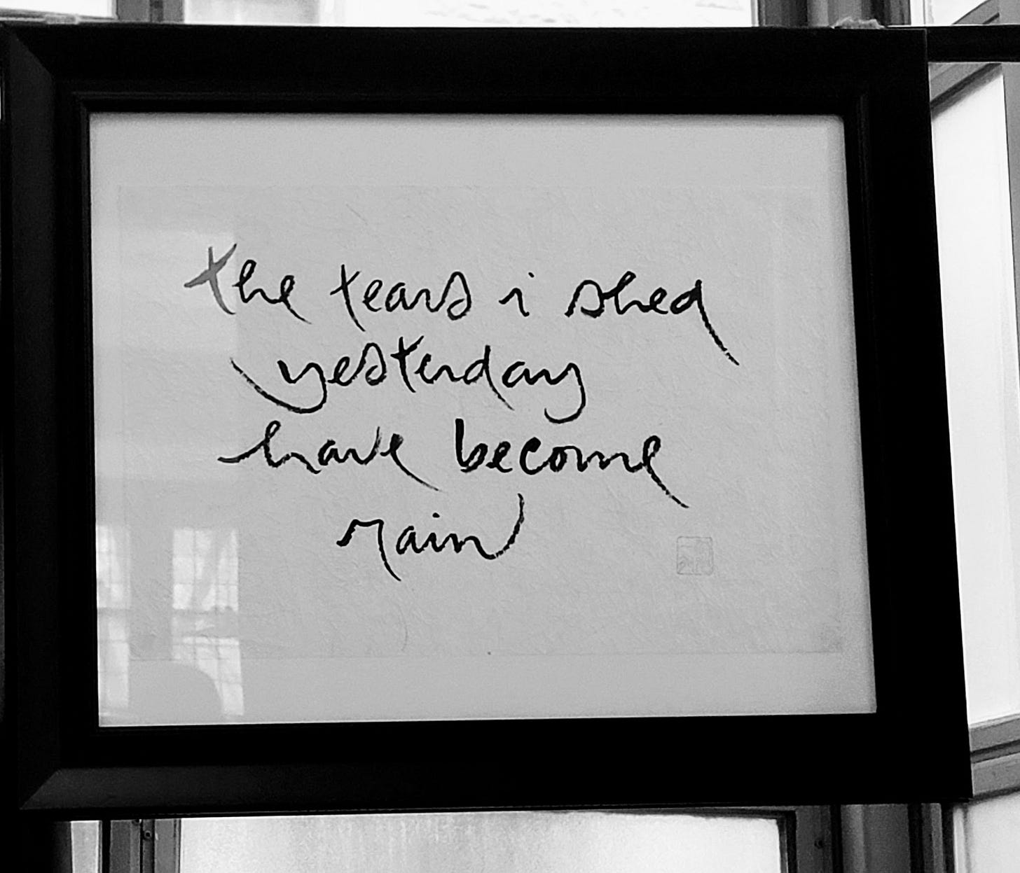 A black and white image of framed calligraphy reading 'the tears i shed yesterday have become rain'