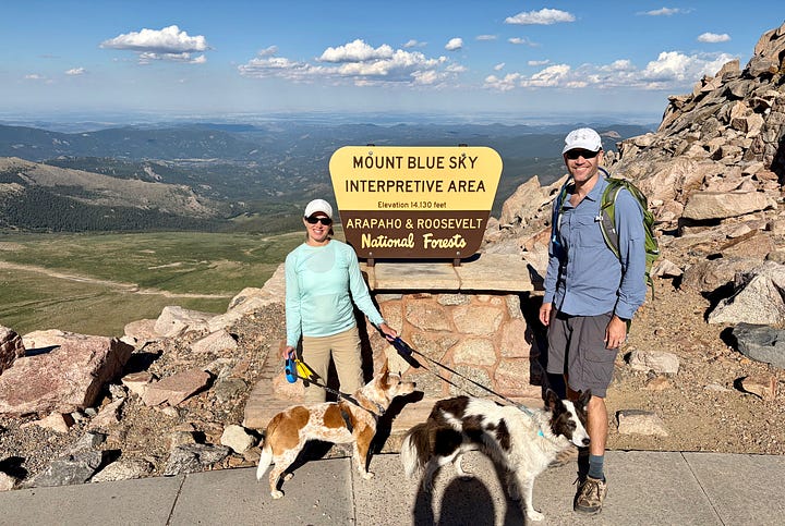 a woman, man and two dogs in front of the Mount Blue Sky sign and two dogs and a man on top of Mount Blue Sky