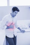 Casual young man with stomach pain standing in the kitchen at home Casual young man with stomach pain standing in the kitchen at home