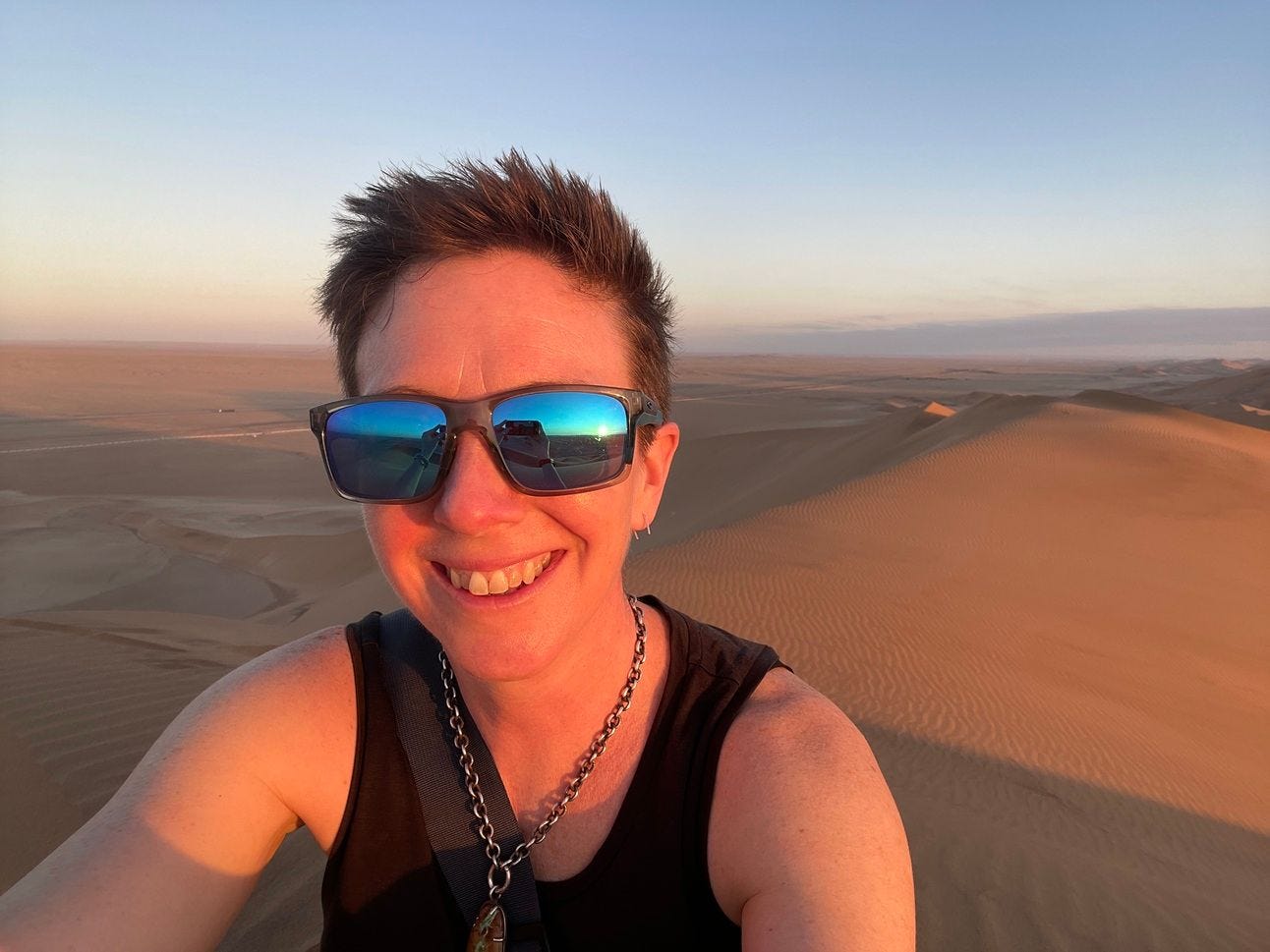 Caroline in sunglasses at the top of sand dunes in Namibia at sunset