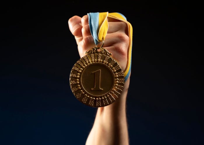 Image of a fist holding a ribbon attached to a gold medal inscribed with '1'