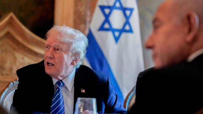 Donald Trump speaks while seated next to Benjamin Netanyahu, with an Israeli flag visible in the background.