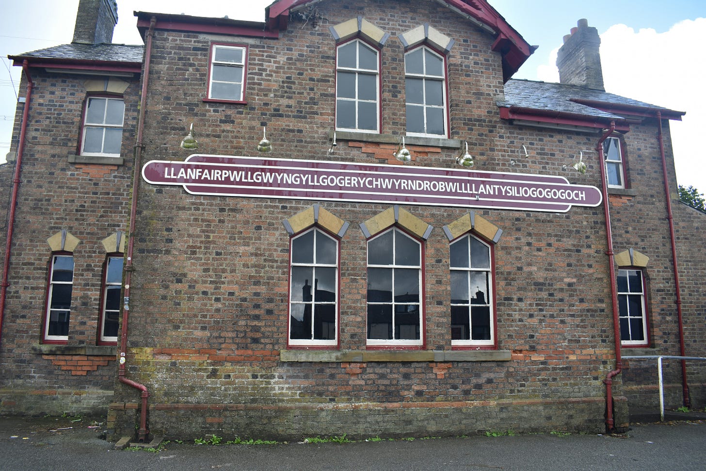 A brown brick building with a brown and white railway sign that reads "llanfairpwllgwyngyllgogerychwyrndrobwllllantysiliogogogoch"
