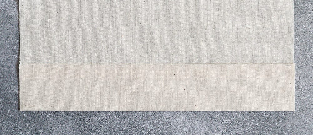 Cream muslin fabric with hem folded up and slip stitched in place.