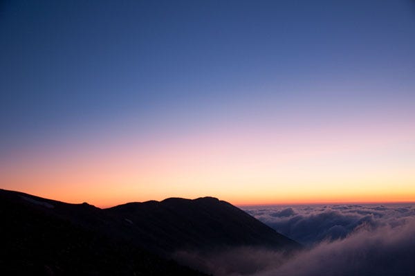 Dark blue indigo sky offset a balck mountain range in the foreground. There is a orange glow from teh setting sun. Dark blue indigo sky offset a balck mountain range in the foreground. There is a orange glow from teh setting sun.