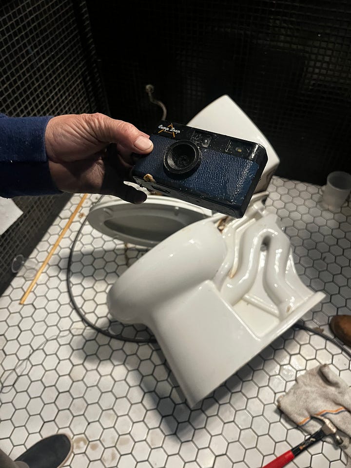 A toilet broken to reveal a plastic camera, the plastic camera being held in front of the toilet