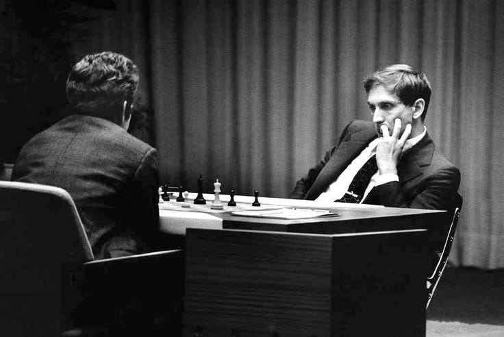 This may contain: two men sitting at a table with chess pieces on the table in front of them This may contain: two men sitting at a table with chess pieces on the table in front of them