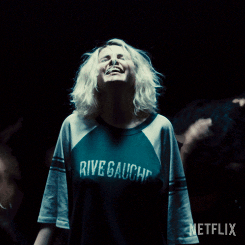 a woman wearing a rive gauche shirt is laughing in the dark