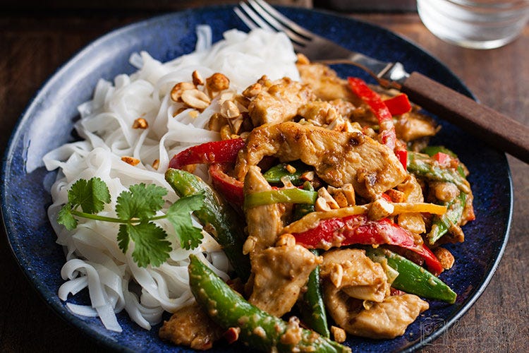 Nutty chicken stirfry on plue plate served with rice noodles.