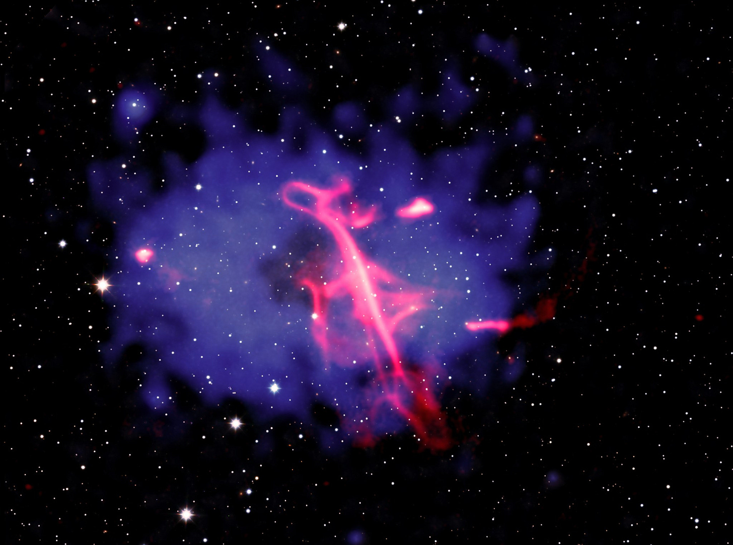 A composite image of a remarkable radio wave formation that strongly resembles a treble clef musical symbol, hovering in the midst of two colliding galaxy clusters. Here, galaxies in the galaxy clusters, plus foreground and background stars and galaxies, blanket the image with specks of light set against the blackness of space. At the center of the frame is a large, oval, blue-purple cloud with ragged edges. In the middle of the purple field, tilting slightly to our left, is what appears to be a giant treble clef, loosely drawn with a neon pink marker. Like the musical notation for which it's named, the formation has a strong vertical stroke with a continuous, fluid line swooping back and forth as it moves from top to bottom. A composite image of a remarkable radio wave formation that strongly resembles a treble clef musical symbol, hovering in the midst of two colliding galaxy clusters. Here, galaxies in the galaxy clusters, plus foreground and background stars and galaxies, blanket the image with specks of light set against the blackness of space. At the center of the frame is a large, oval, blue-purple cloud with ragged edges. In the middle of the purple field, tilting slightly to our left, is what appears to be a giant treble clef, loosely drawn with a neon pink marker. Like the musical notation for which it's named, the formation has a strong vertical stroke with a continuous, fluid line swooping back and forth as it moves from top to bottom.