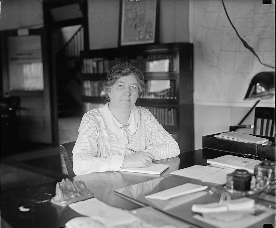 Black and white photograph of a woman sitting at a desk with pencil in hand.