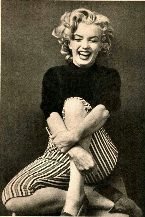 This may contain: marilyn monroe laughing while sitting on the floor with her legs crossed and hands folded over her chest