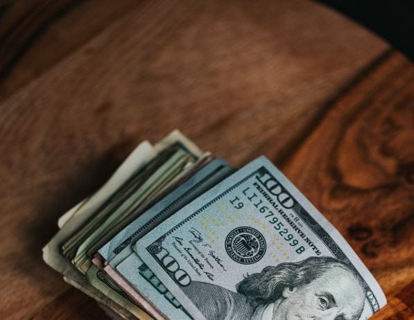 A stack of hundred-dollar bills placed on a wooden surface, symbolizing financial success and monetization.