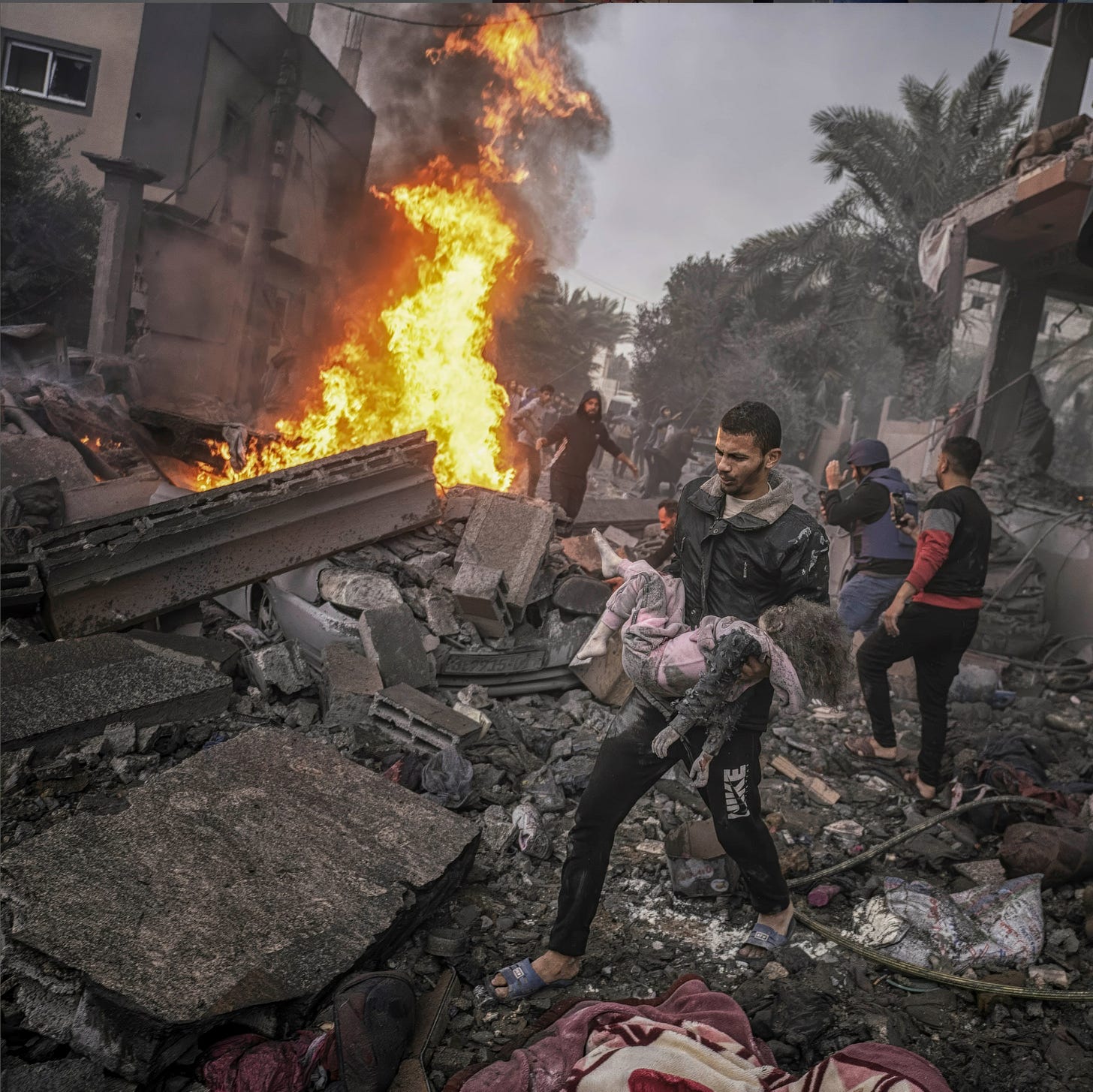 On the fifth of last December, I took this photo of my neighbor Suhaib, who is only 18 years old, as he is carrying a little girl who got killed in Israeli bombing of our neighbors’ house. I just learned that Suhaib was killed by an Israeli drone missile in front of their house with four others from his family.