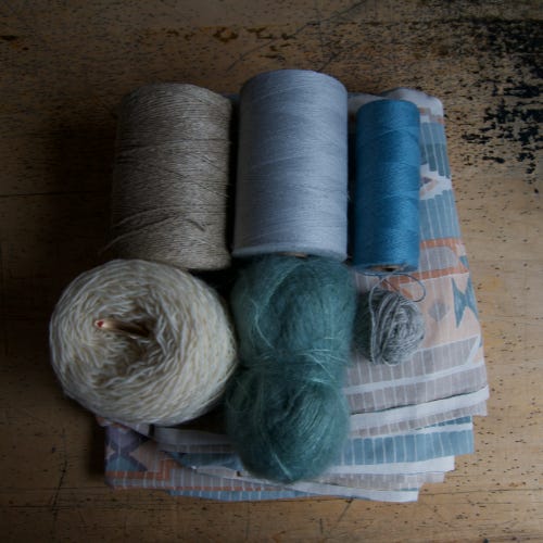Tubes and balls of colourful yarn lie on top of a patterned cloth