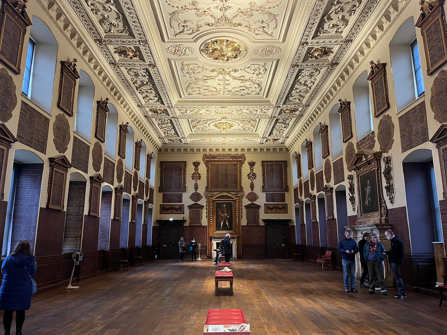 An elaborate ballroom with names inscribed all over the walls and a few portraits hanging. Some benches sit on the otherwise empty floor, and a few people mill about. An elaborate ballroom with names inscribed all over the walls and a few portraits hanging. Some benches sit on the otherwise empty floor, and a few people mill about.