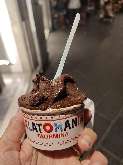 View of Mount Etna, misty in the distance from the Greek Theatre, Taormina; a tub of vegan chocolate gelato, Taormina, bubble car with colourful traditional Sicilian decoration parked in front of a church in Taormina, Sicily