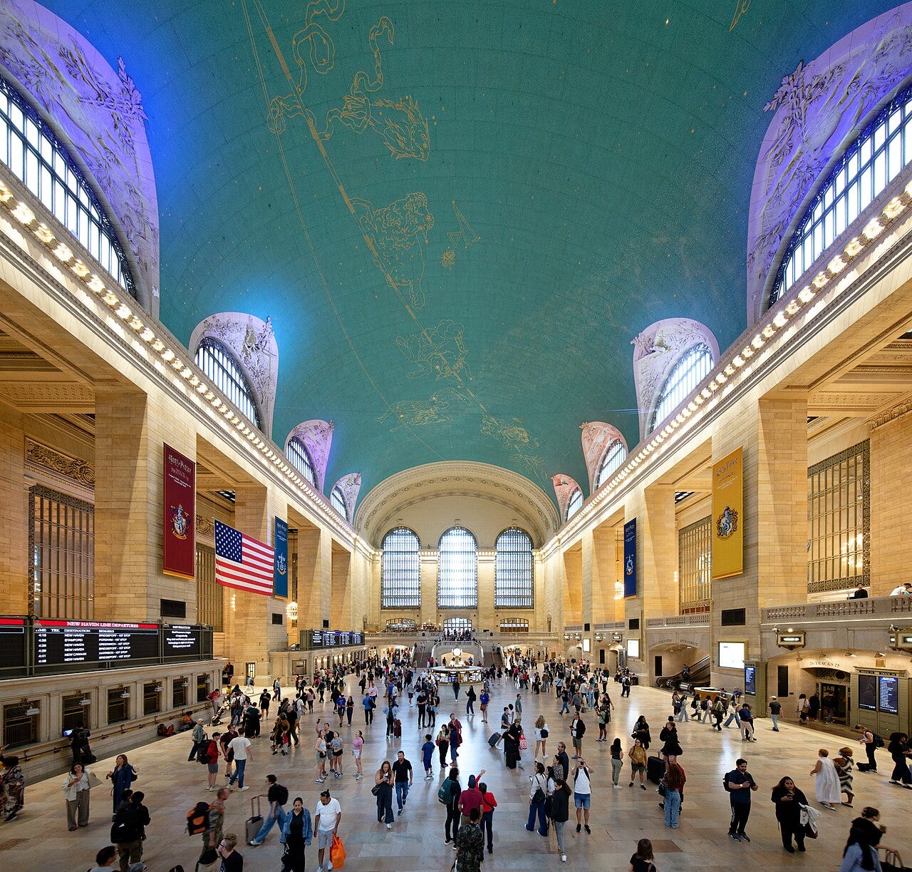 The blue-green ceiling of the Main Concourse of Grand Central Terminal with gold constellations, seen above the crowd