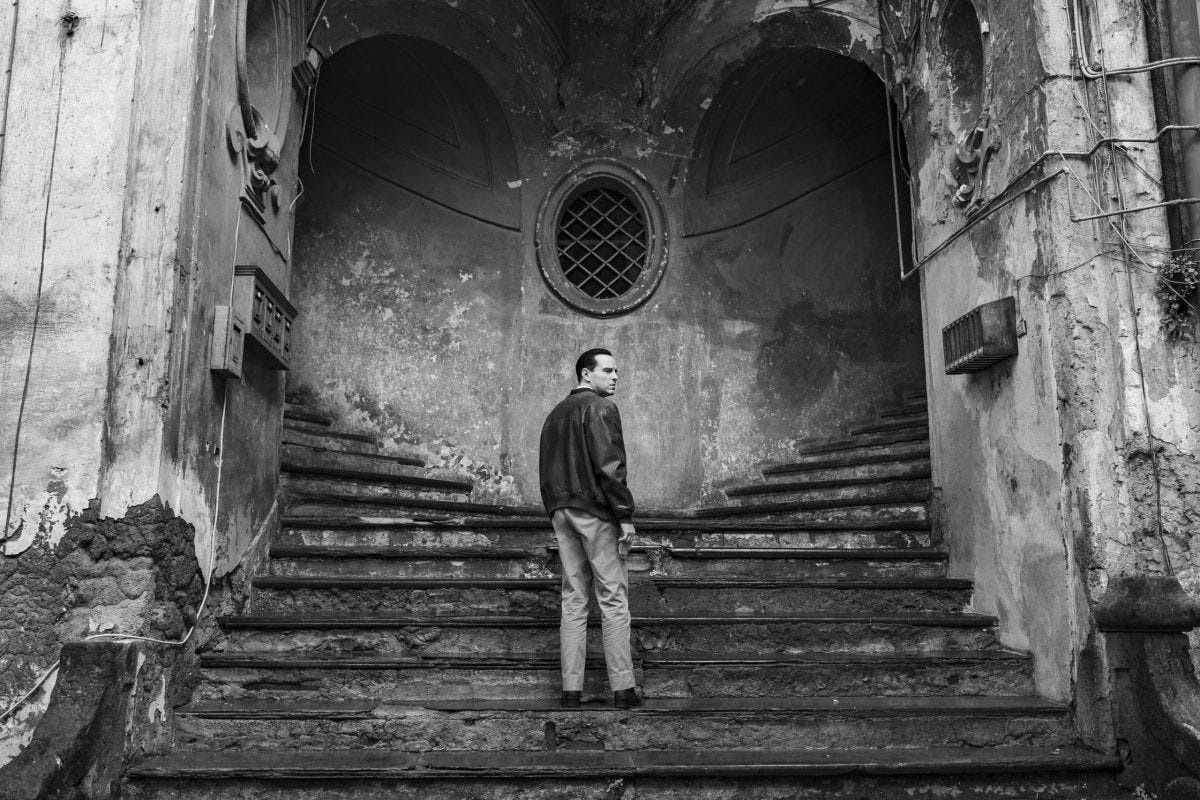 A white man in a leather jacket contemplating which old stone staircase to descend