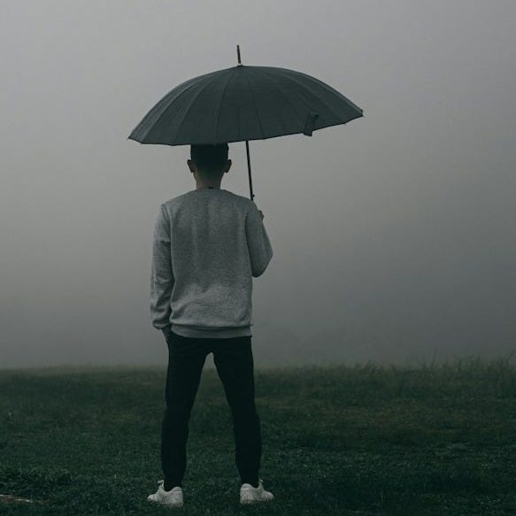 person in white jacket and gray pants holding umbrella standing on foggy field