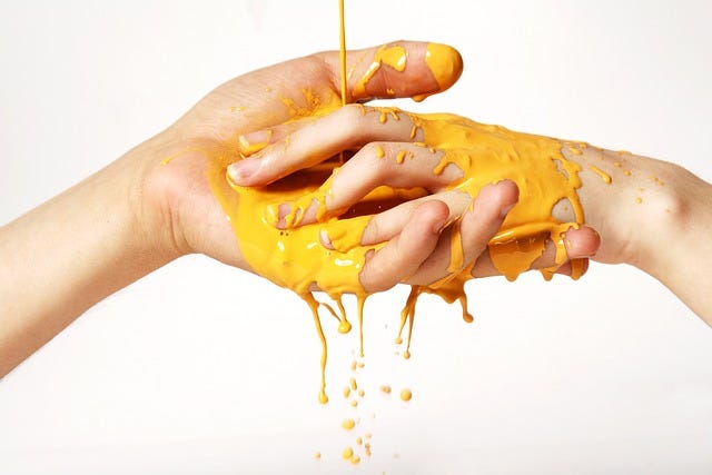 two hands grip, touch, while yellow paint pours onto them two hands grip, touch, while yellow paint pours onto them