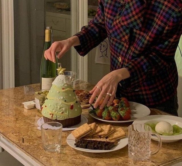 This may contain: a woman in a plaid coat is cutting up food on a table with wine bottles and glasses