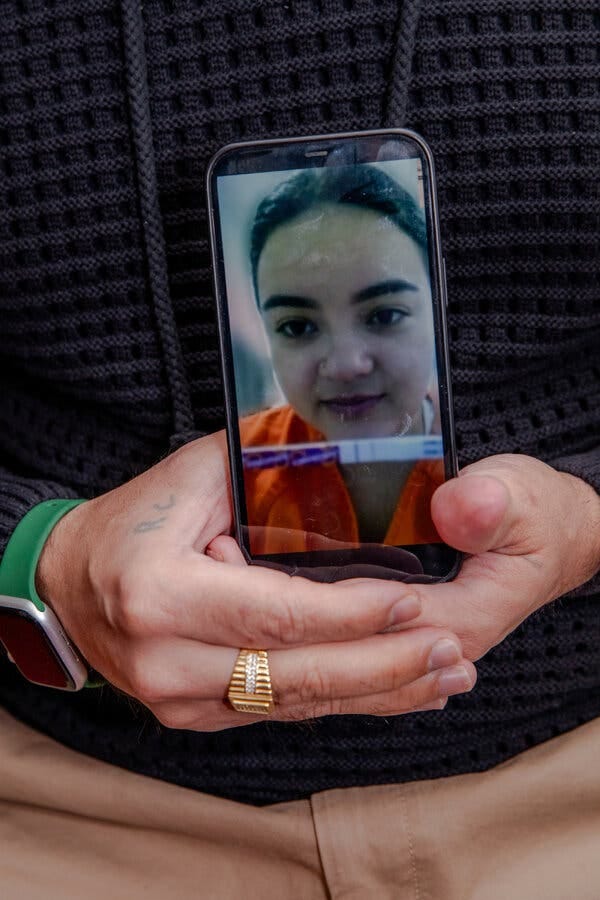A man’s hands holding a mobile phone showing a woman in an orange jumpsuit with a pregnancy test.
