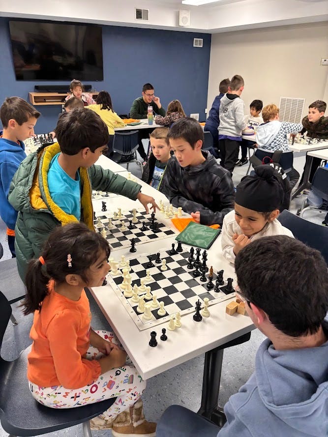 A group of children gather around tables, set with chess boards. A group of children gather around tables, set with chess boards.