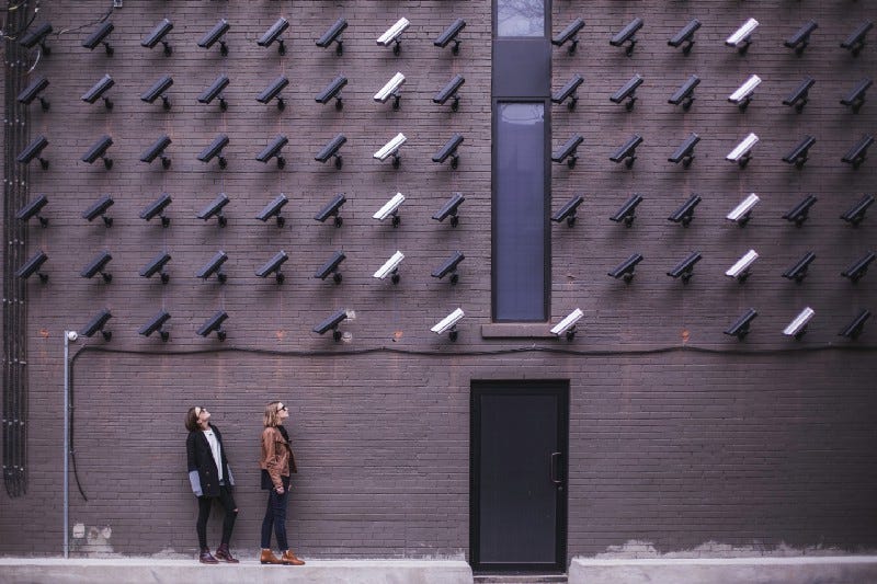 Two women looking up at a brick wall of fifty CCTV cameras. Two women looking up at a brick wall of fifty CCTV cameras.