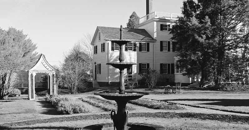 A black and white image showing a fountain with the Strawbery Banke Museum in the background