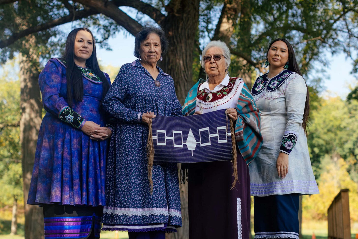 Haudenosaunee women in wampum-coloured traditional dress hold a glass replica of the Hiawatha Belt. Left to right: Karissa John (Mohawk), Clan Mother Mary Sandy (Oneida), Elder Norma Jacobs (Cayuga), Makasa Looking Horse (Mohawk/ Lakota). Haudenosaunee women in wampum-coloured traditional dress hold a glass replica of the Hiawatha Belt. Left to right: Karissa John (Mohawk), Clan Mother Mary Sandy (Oneida), Elder Norma Jacobs (Cayuga), Makasa Looking Horse (Mohawk/ Lakota).