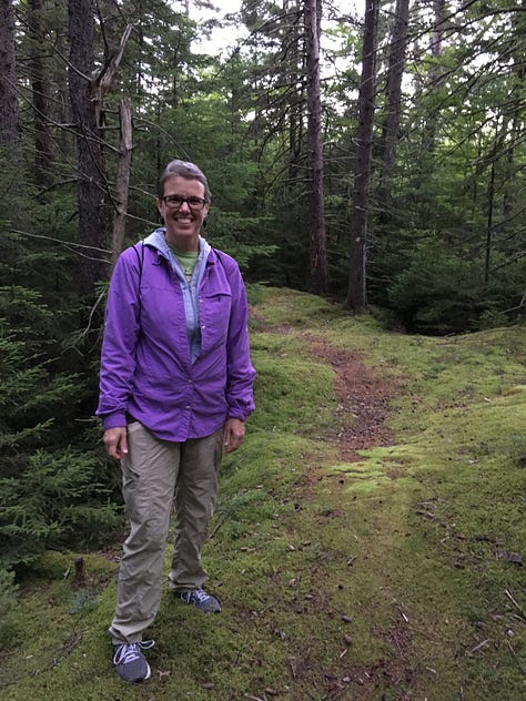 girl and dad with backpacks on in front of stream, two women by trailhead sign in forest, solo woman beside mossy trail