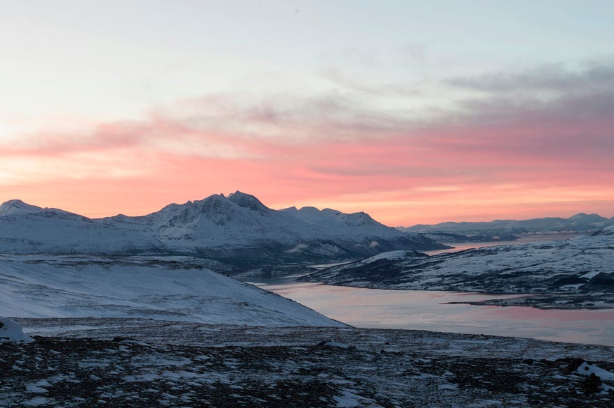 A snow covered fjord at sunset.