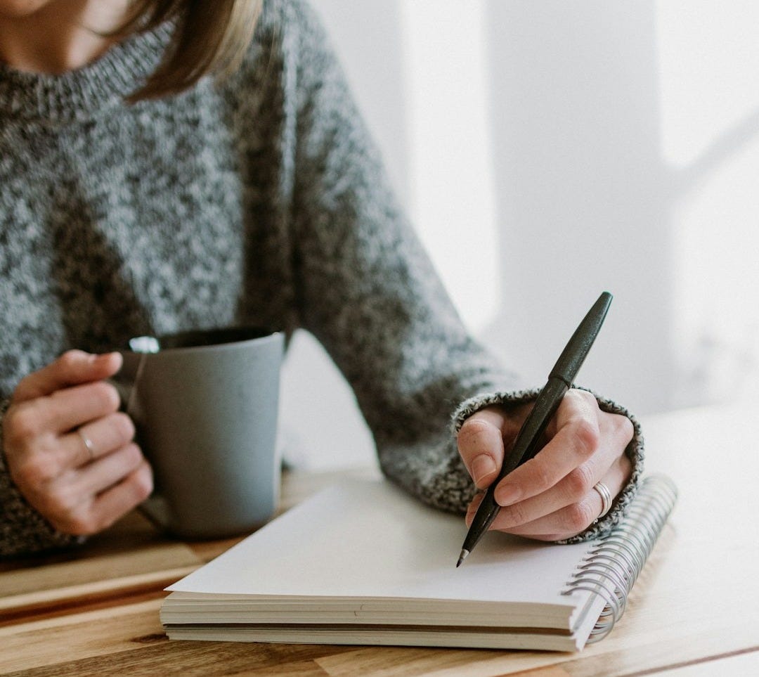 a woman sitting at a table writing on a notebook a woman sitting at a table writing on a notebook