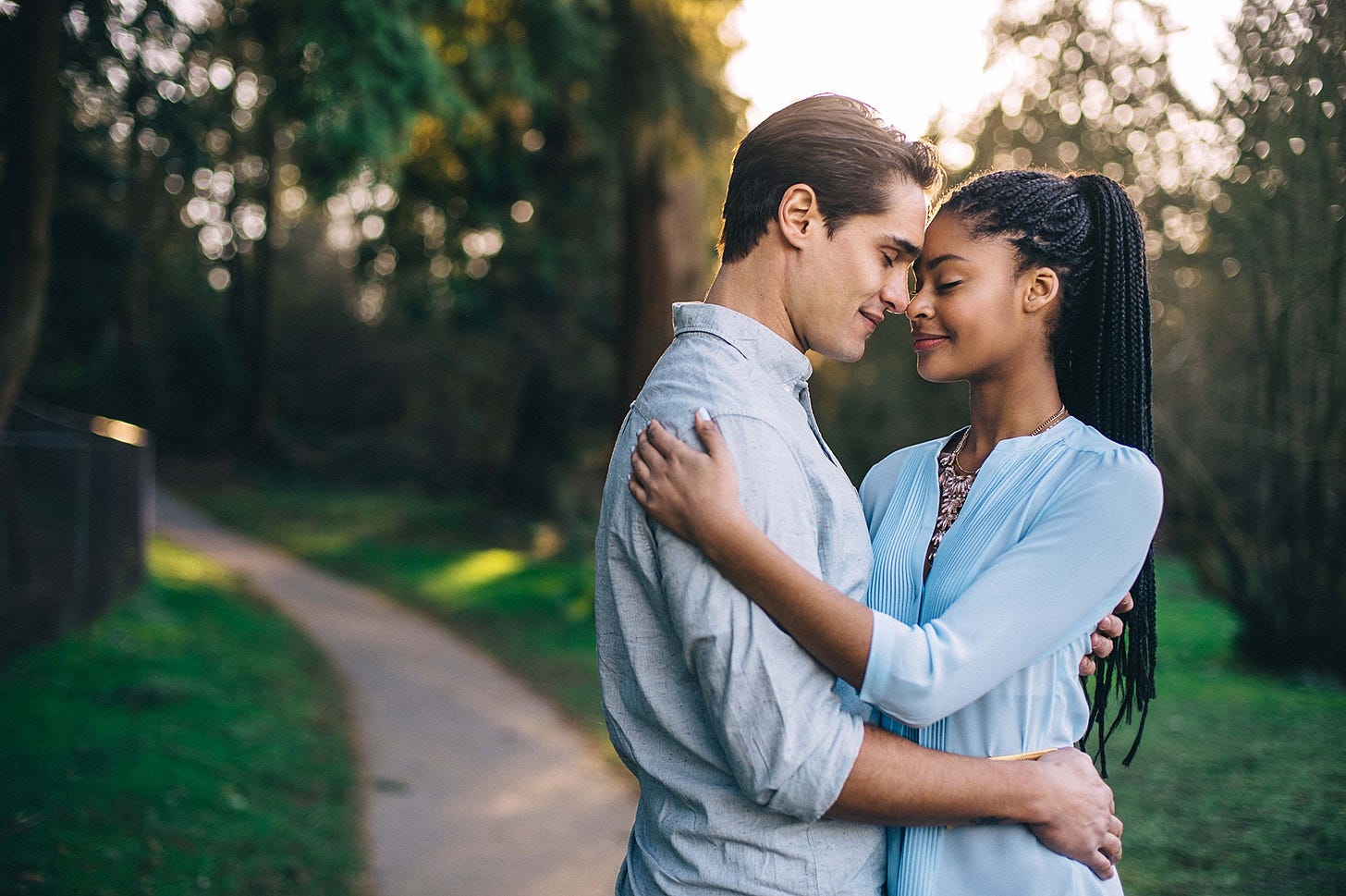 A handsome couple embraces lovingly on a sunlit park path.