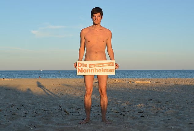 Councilor Julien Ferrat, nude, holds a sign that reads “Die Mannheimer”