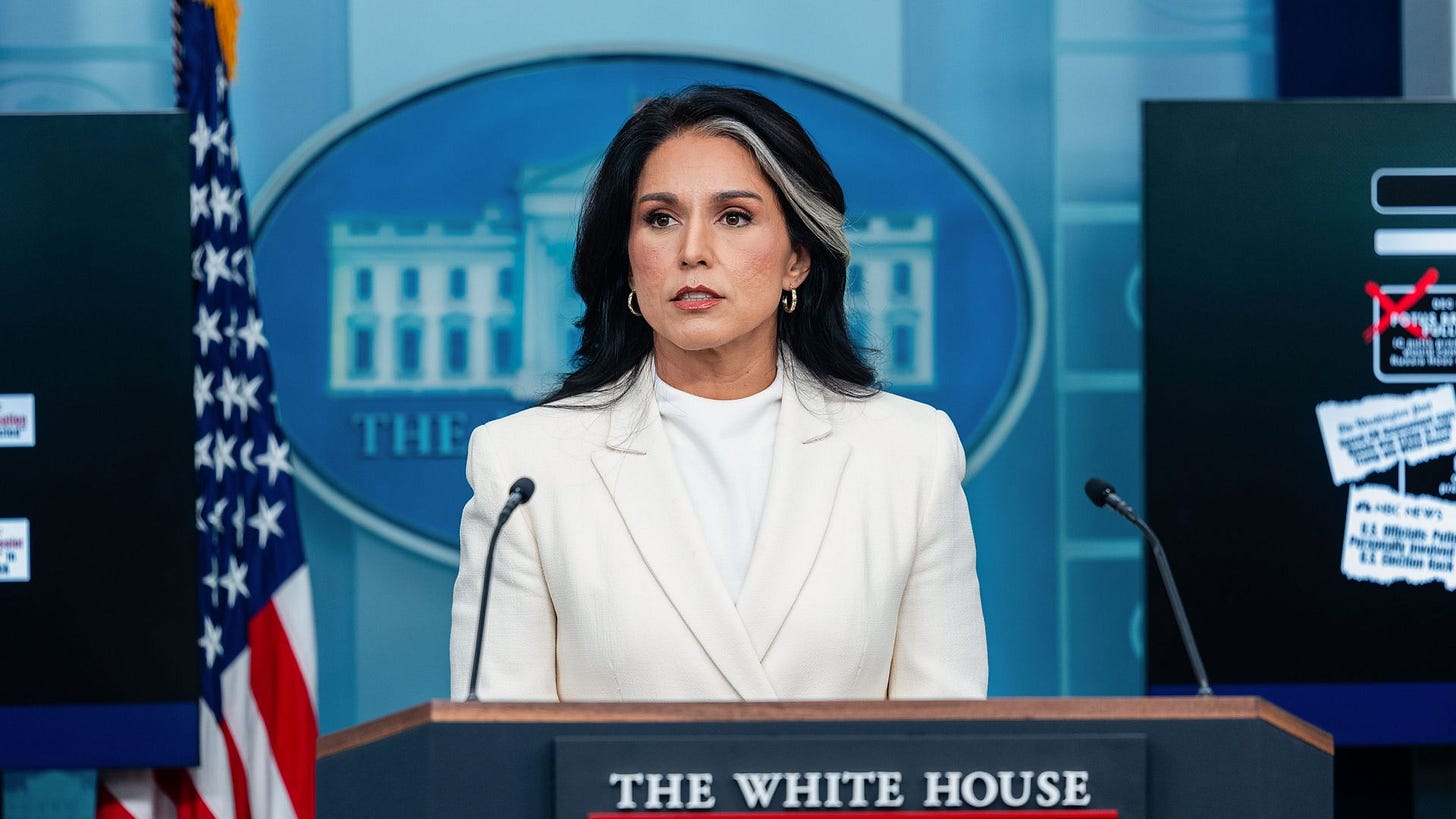 Tulsi Gabbard, wearing all white, speaks from a podium in the White House press briefing room.