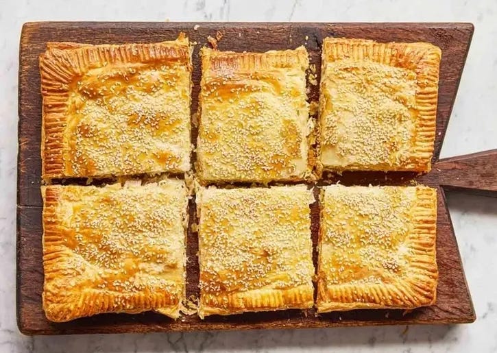 Creamy chicken and chive pie sliced into six pieces topped with sesame seeds on a wooden board