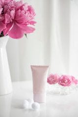 pink tube of skincare with cotton balls next to pink flowers