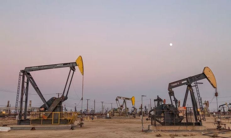This may contain: several oil pumps in the middle of an open field at dusk, with one being used as a fuel pump