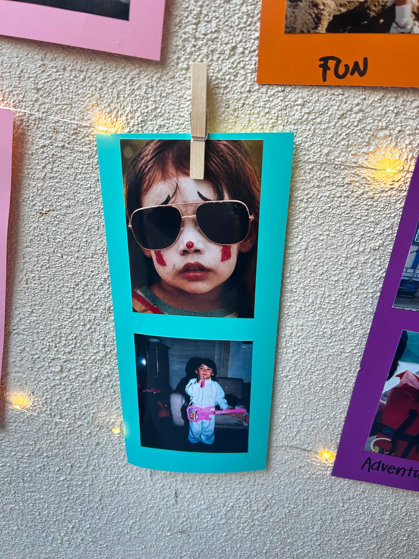 two photographs are on a clothesline with bright blue paper behind the photos. One shows the close up of a little girl's face in oversize sunglasses and clown makeup. The photogtaph below has a little brown girl with a mic in her hand and a pink toy guitar two photographs are on a clothesline with bright blue paper behind the photos. One shows the close up of a little girl's face in oversize sunglasses and clown makeup. The photogtaph below has a little brown girl with a mic in her hand and a pink toy guitar