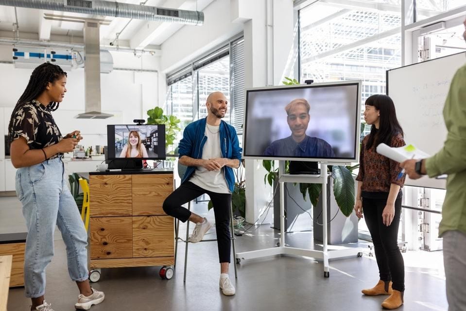 Professional workers collaborating in a modern office using AI-enabled hybrid meeting technology with remote participants on video screens Professional workers collaborating in a modern office using AI-enabled hybrid meeting technology with remote participants on video screens
