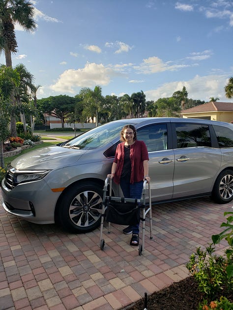 There are 3 photos in a gallery. From left to right: the first photo is the back of a white SUV, but it has been modified and is higher off the ground than normal; the trunk is open, and a wheelchair ramp extends out the back onto the ground. In the second, a red SUV similar to the first in that it has been modified; this view shows the interior of the back, with a built-in wheelchair ramp. The third is a picture of the writer of this piece; she is standing in a driveway with a walker, wearing a burgundy cardigan, black tank top, jeans, one sneaker, and one boot on her feet; behind her is a Silver 2023 Honda Odyssey minivan.