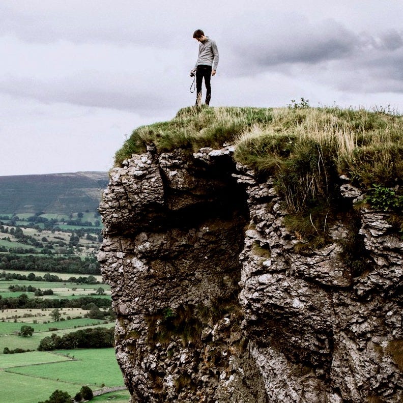man standing on the edge of cliff taken at daytime man standing on the edge of cliff taken at daytime